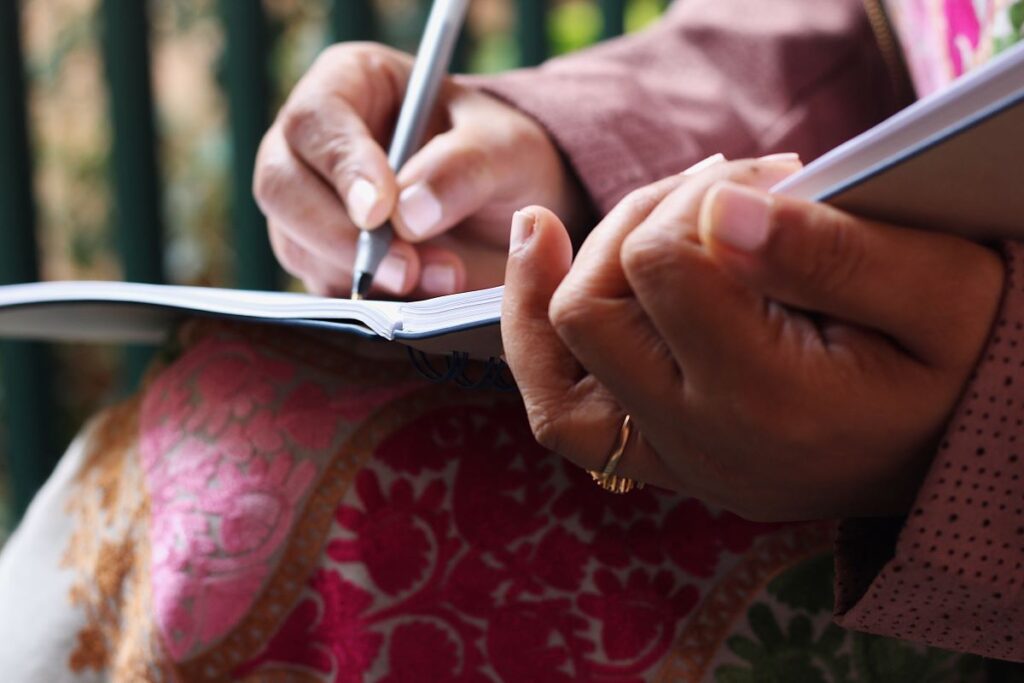 a close up of a woman writing in a notebook with a black pen utilizing valentine's day writing prompts